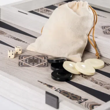 Woreczek z tkaniny, kości i czarno-białe pionki ułożone na planszy do backgammona